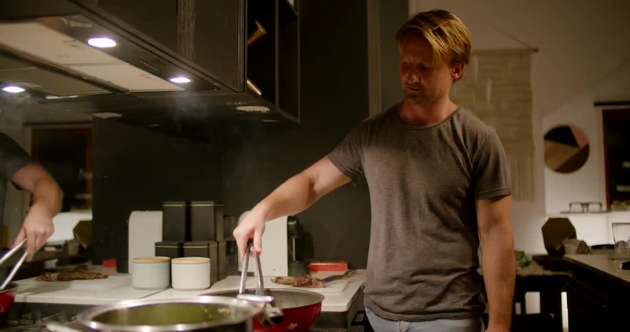 A man nodding and talking while cooking meat in a pan on a stovetop