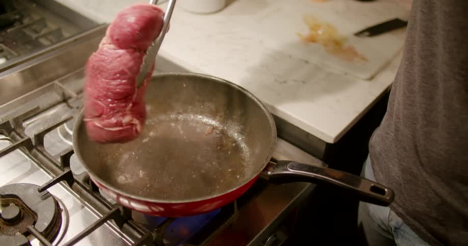 A person cooking steak in a frying pan