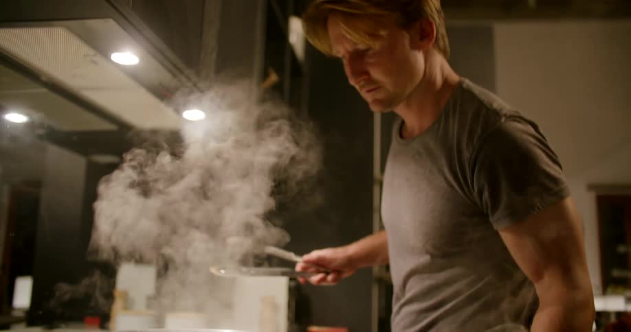 Steam rises as a man opens a pot on the stove while cooking at home