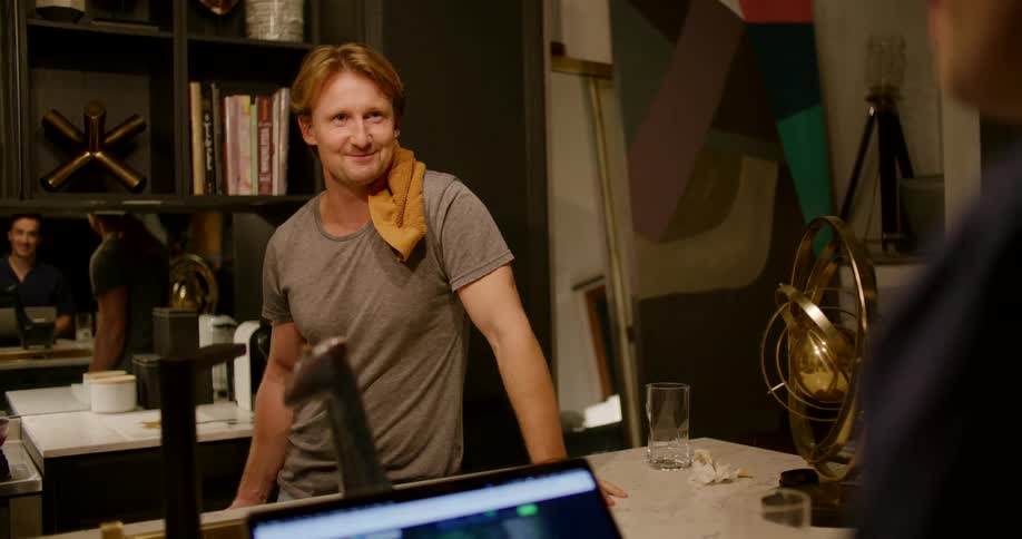 A man slinging a hand towel onto his shoulder while smiling and chatting with a friend