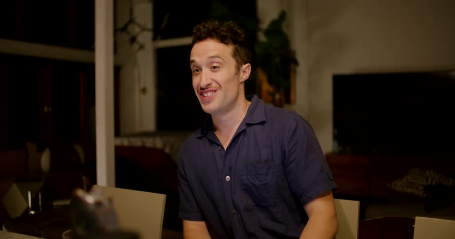 A man laughs while talking to someone while seated in front of a laptop in a conference room