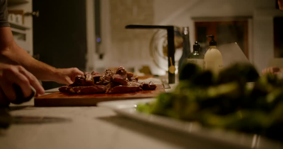 A man carefully slides a cutting board full of steaming hot food onto a kitchen counter