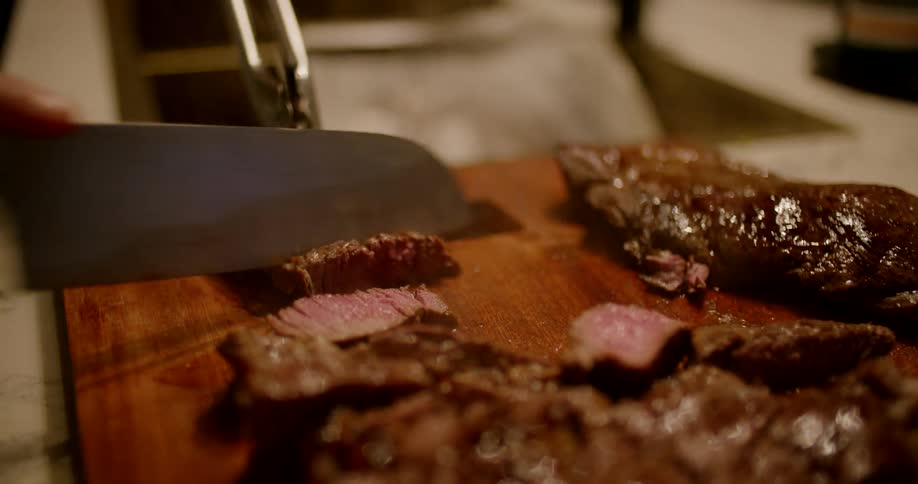 A person is cutting meat with a knife in their kitchen