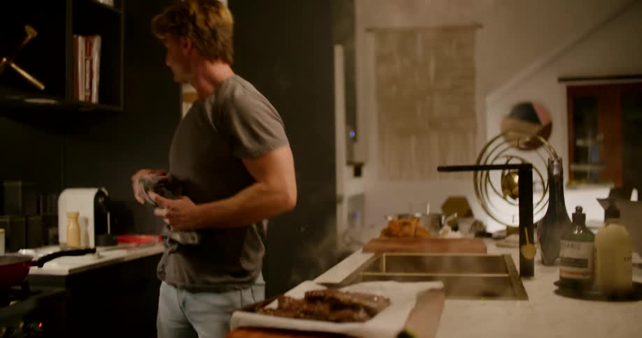 A man uses a towel to pull a hot plate of food from the oven and places it on the cutting board on the counter