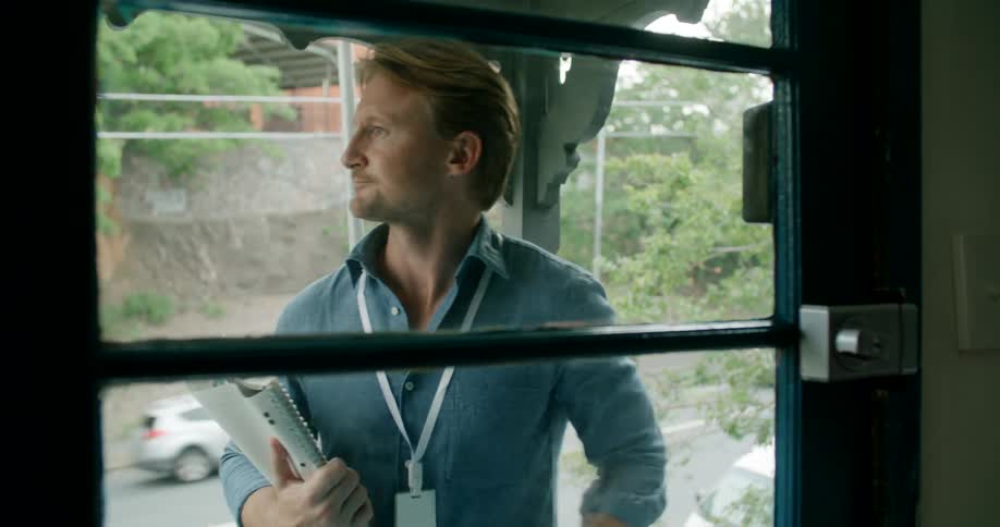 A man carrying a notebook walks up to a house and knocks on a door and a man answers it