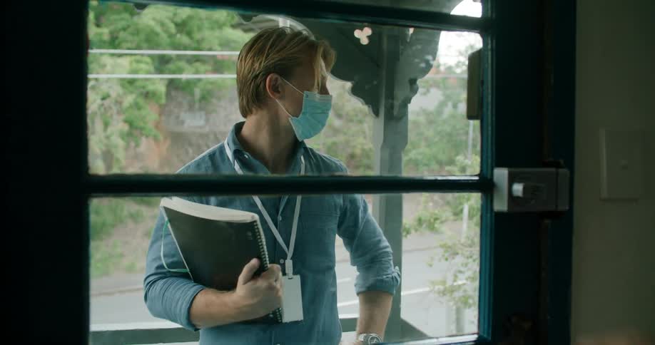 A young fit man wearing a face mask knocks on the door of a house