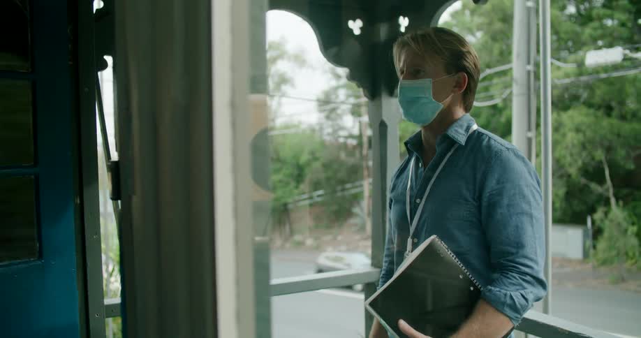 A man walking up to a door and knocking on it while holding a book