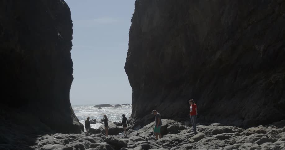 A group of people walking on a rocky shore between two large rock formations