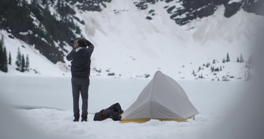 A man standing next to a tent while he photographs the wintry landscape