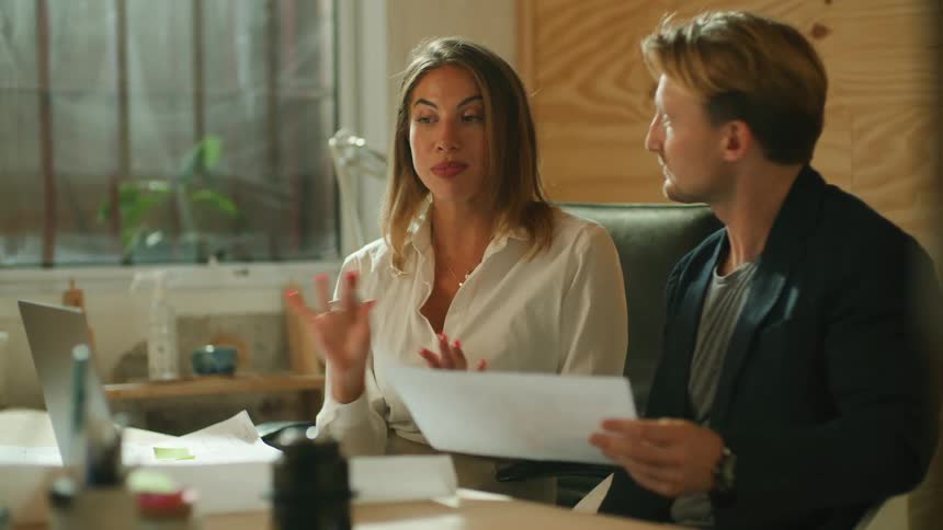 A man reads a piece of paper while listening to his coworker talk