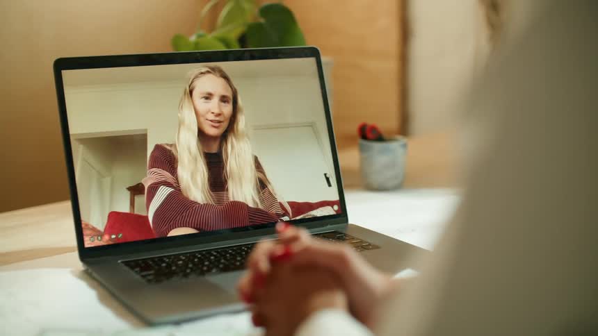 A pair of women talk with each other through video chat on a laptop while sitting indoors