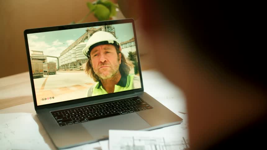 A woman in front of a laptop video chats with a construction worker