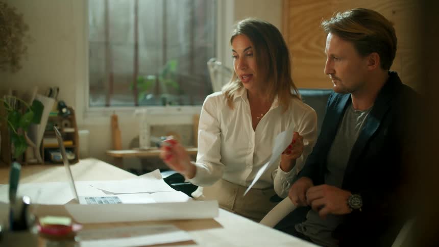 A man and woman coworkers are sitting at the office and talking together