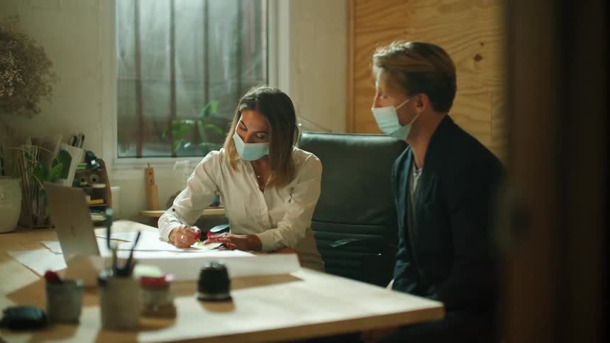 Two coworkers are communicating in an office and wearing face masks