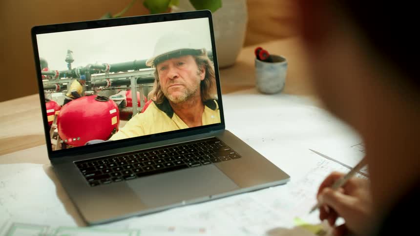 A construction worker with a hard hat talking to a man via video chat