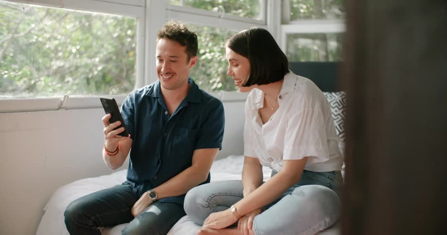 A man and woman are looking at a cellphone while sitting indoors