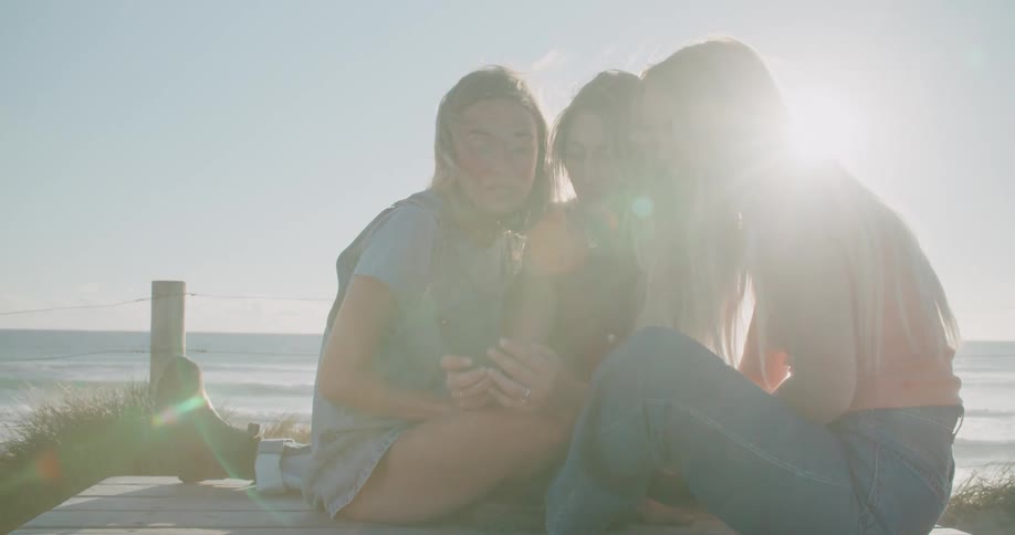 A group of three girls sitting at the beach talking on a phone