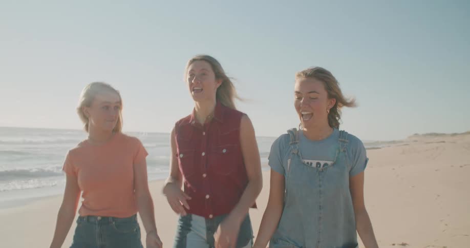 Three girls walk on the beach talking and laughing