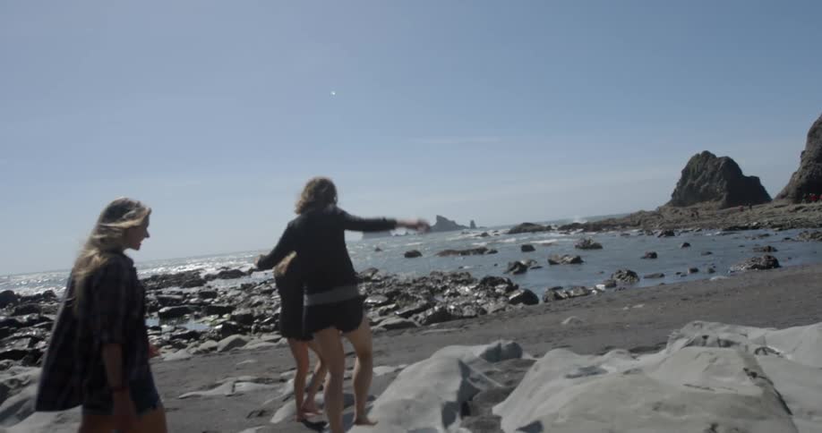 Three women are walking on some rocks by the beach