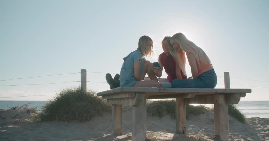 Three women look at a phone on the beach