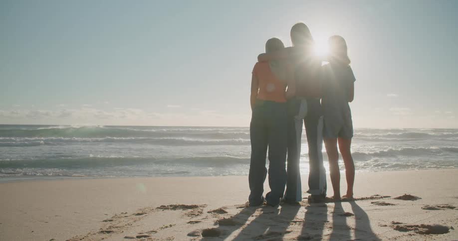 The women stand close together on the beach