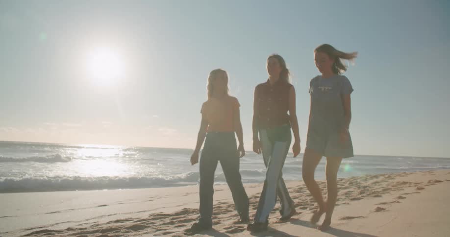 A trio of teenage females walk together along the beach on a very sunny day