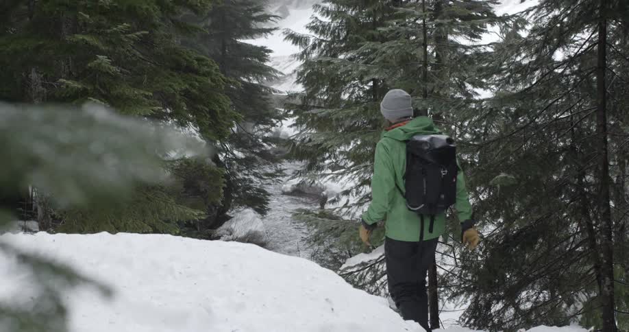 A person is hiking in the snow by a stream
