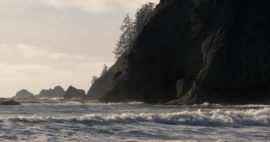 Waves crash on a beach near a rocky hill
