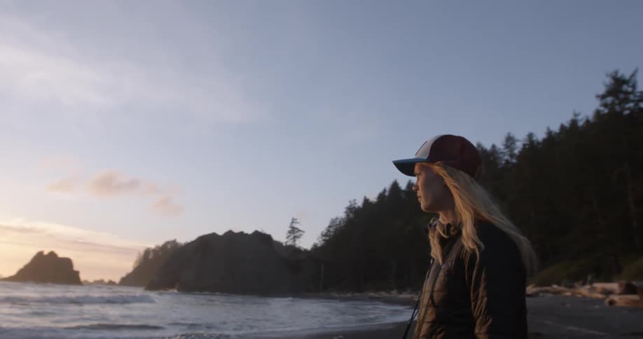 A woman is looking over the water towards a sunset