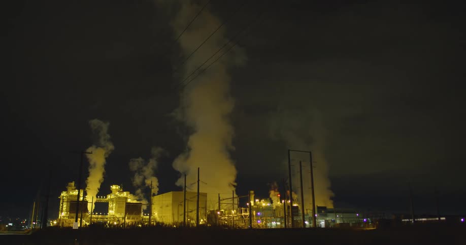 The exterior of an industrial area with lights and smoke or steam at night