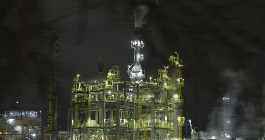 An oil refinery with lights smoke and chimneys with the sky in the background