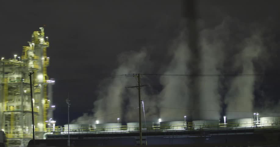 Smoke rises from metal silos at a refinery