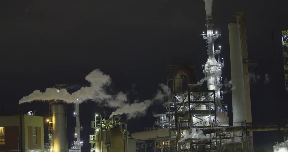 The exterior of an industrial area at night with lights and smoke