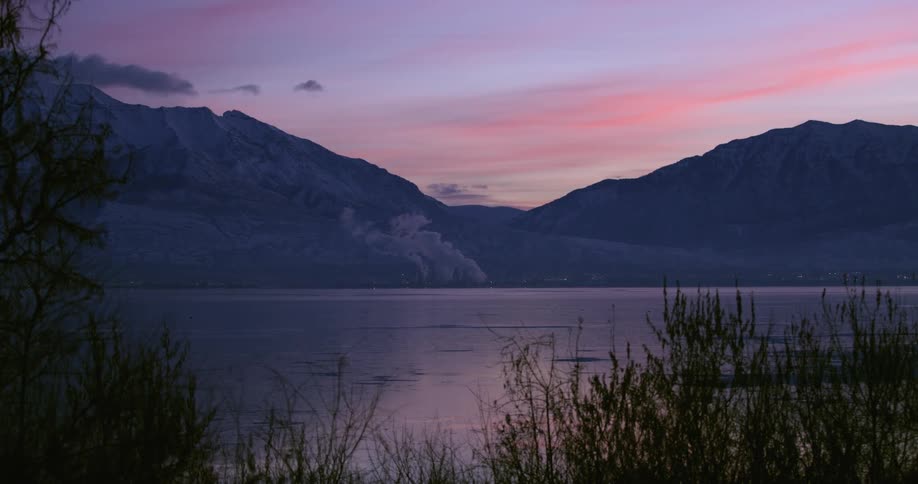 River with grass around and mountains behind it with pink clouds in the sky