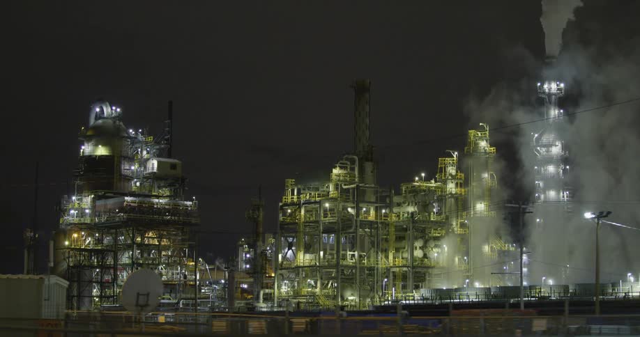 Smoke and steam rise from an oil refinery located off a highway