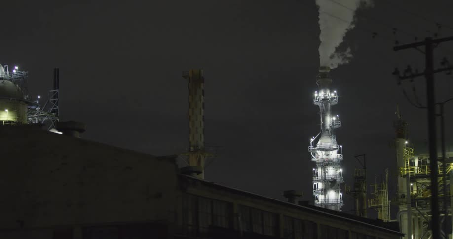 Smoke billows into the night sky from the smokestack of a factory