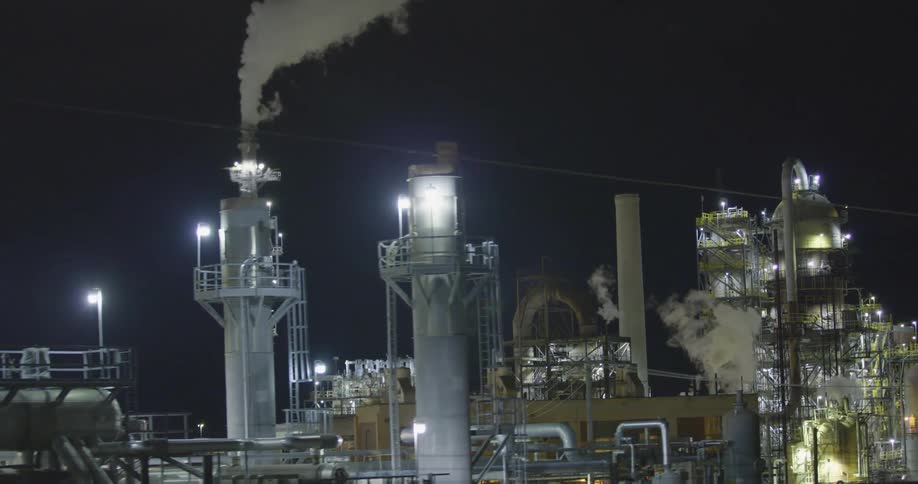 An industrial area with lights chimneys and smoke against the night sky