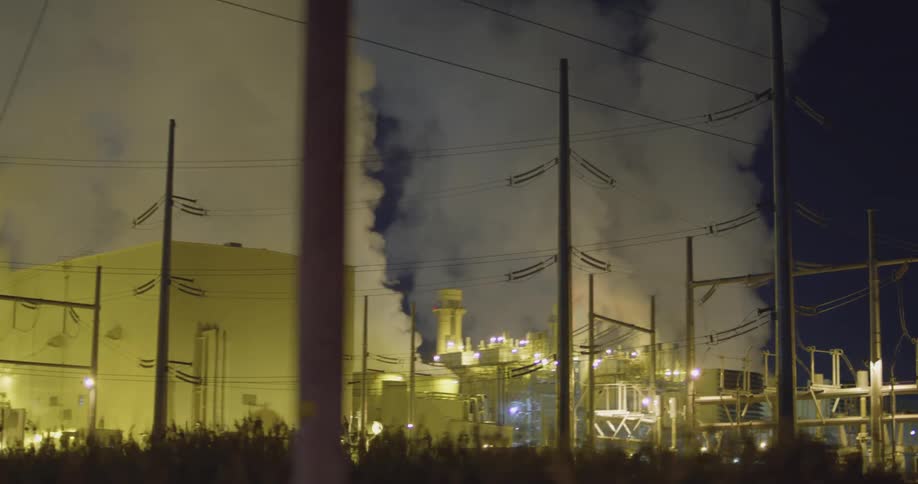 Industrial building with lights smoke and chimneys with the sky in the background