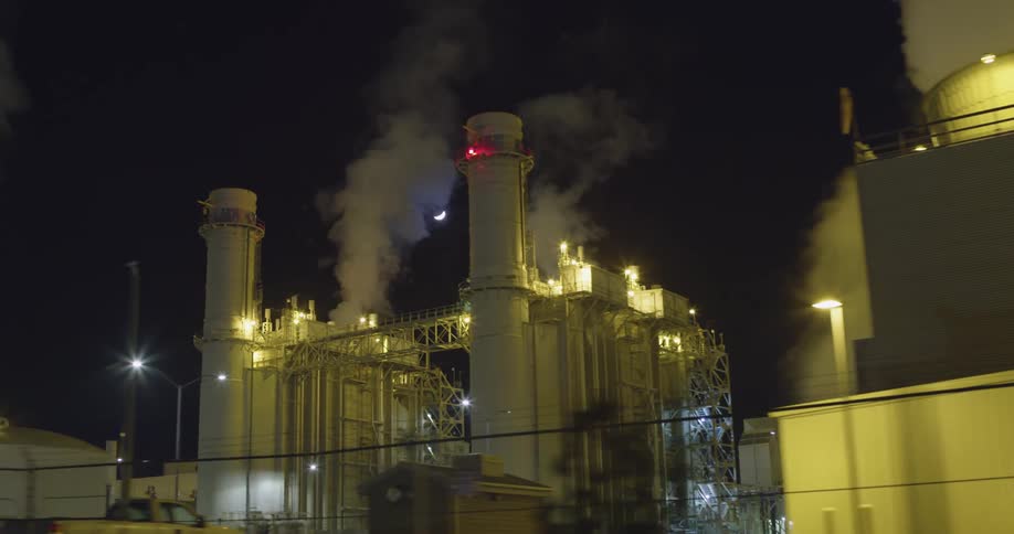 Smoke rising from industrial area at night with crescent moon in sky