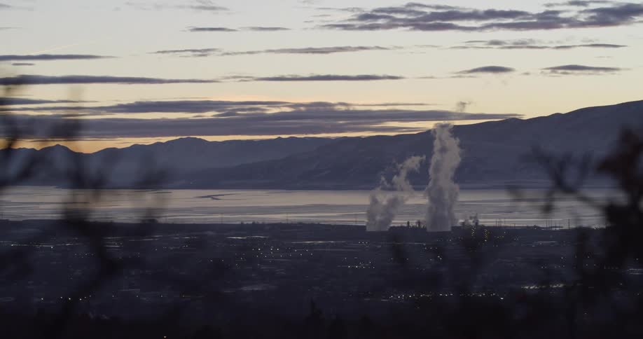 An aerial view of smoke billowing out of a factory on the shoreline
