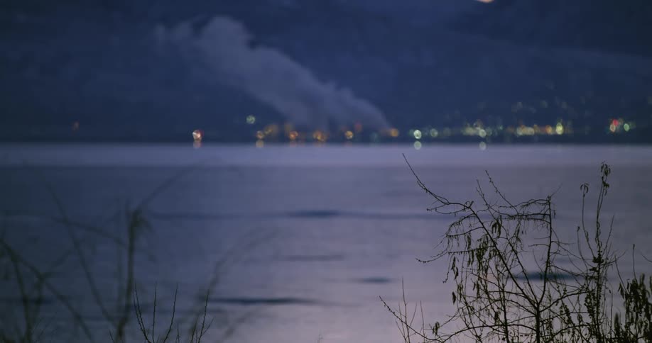 Clouds of steam and vapor rising from a power plant in a small town in the coast of a lake at dawn