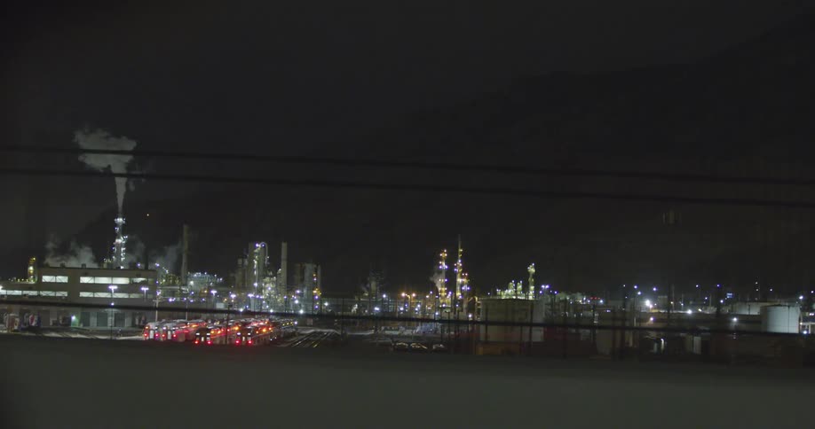 A landscape view of a refinery with a city skyline in the background