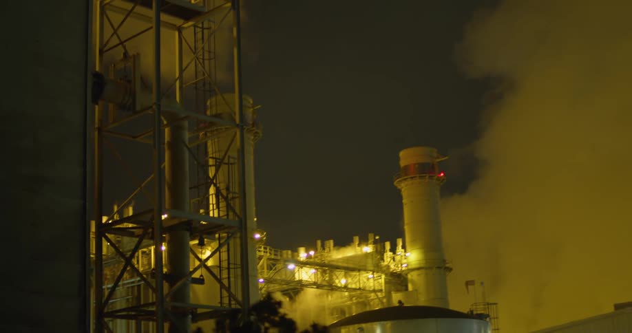 A power plant with lights chimneys and smoke with the sky in the background