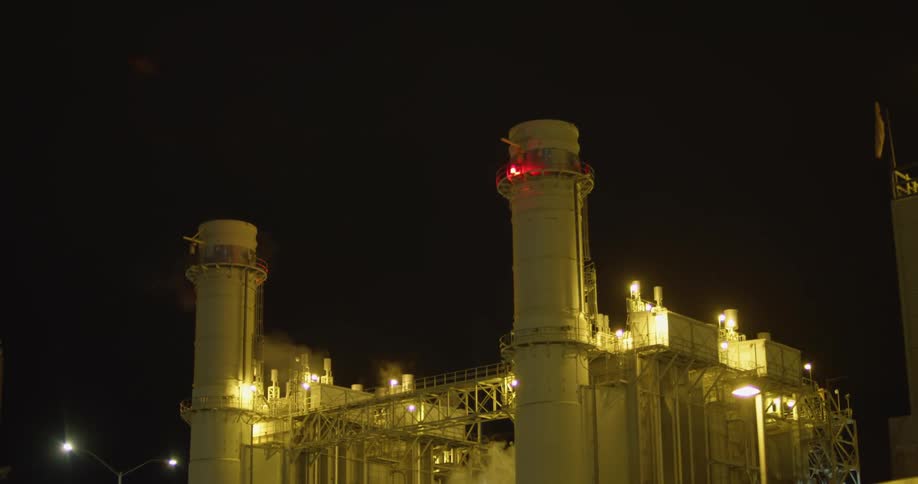 The exterior of a power plant at night with red and white lights shining