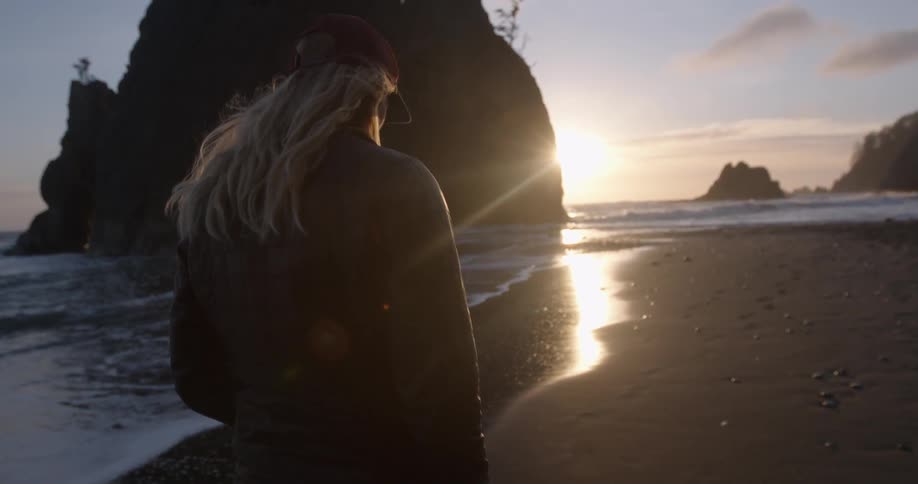 A woman walks on a beach at sunset