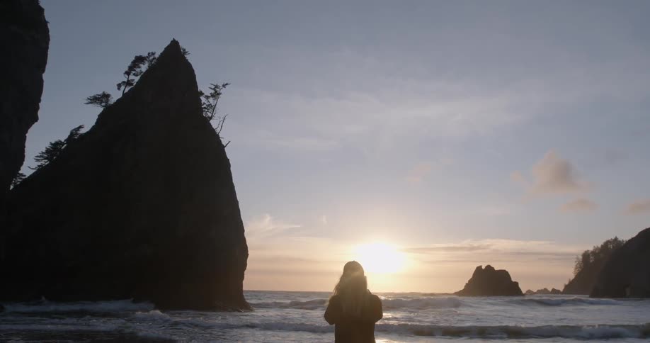 A person is standing by the beach watching the sunset