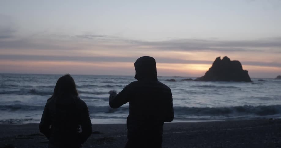 A man and woman chatting on a beach during a chilly sunset