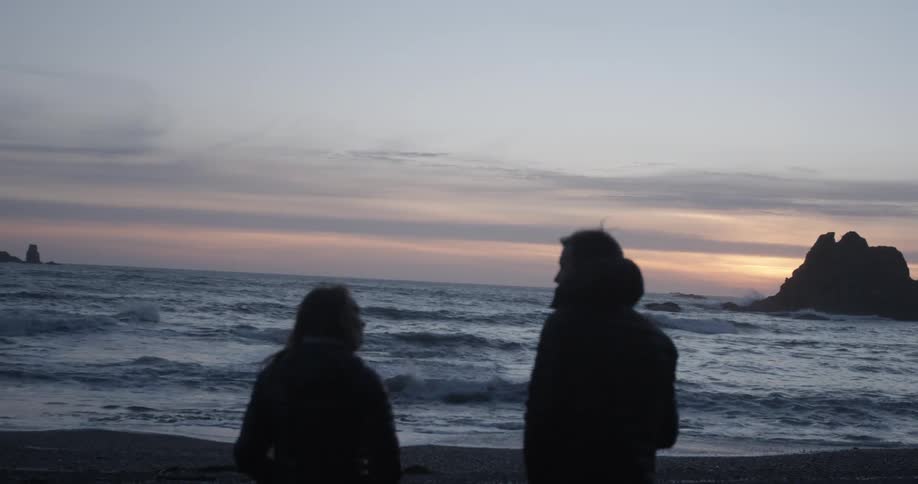 A man and woman chatting on the coastline during sunset