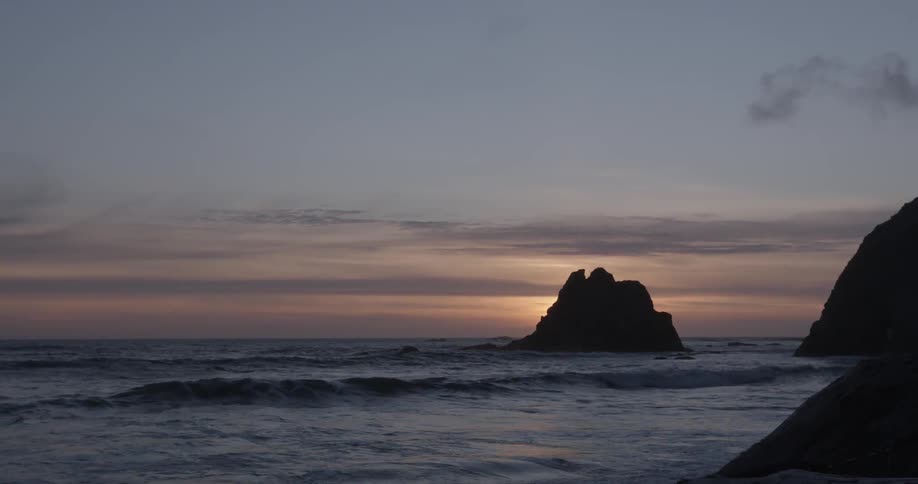 Waves flowing around rock formations and towards shore at sunset