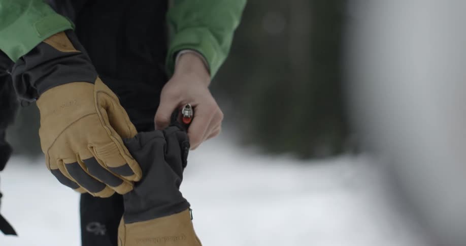 A man wearing a winter coat rises from a squatting position and leaves a lighter on the ground